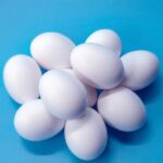 Uova su un piatto con un misurino e un grafico sul colesterolo sullo sfondo.